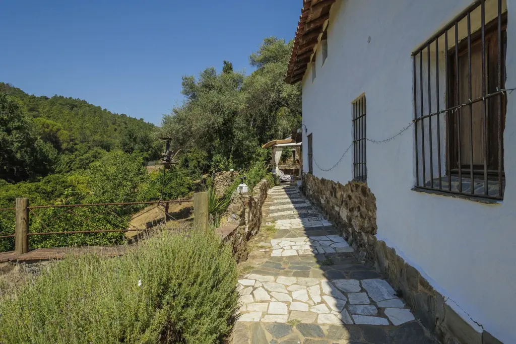 Sendero empedrado junto a la fachada encalada de la casa rural, con rejas y jardín