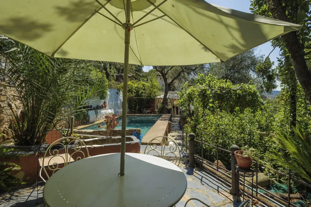 Terraza con mesa y sombrilla sobre la piscina de la casa rural