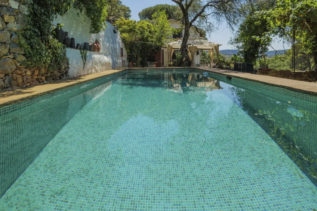 Piscina alargada con muro encalado y cenador al fondo, en la Sierra de Aracena