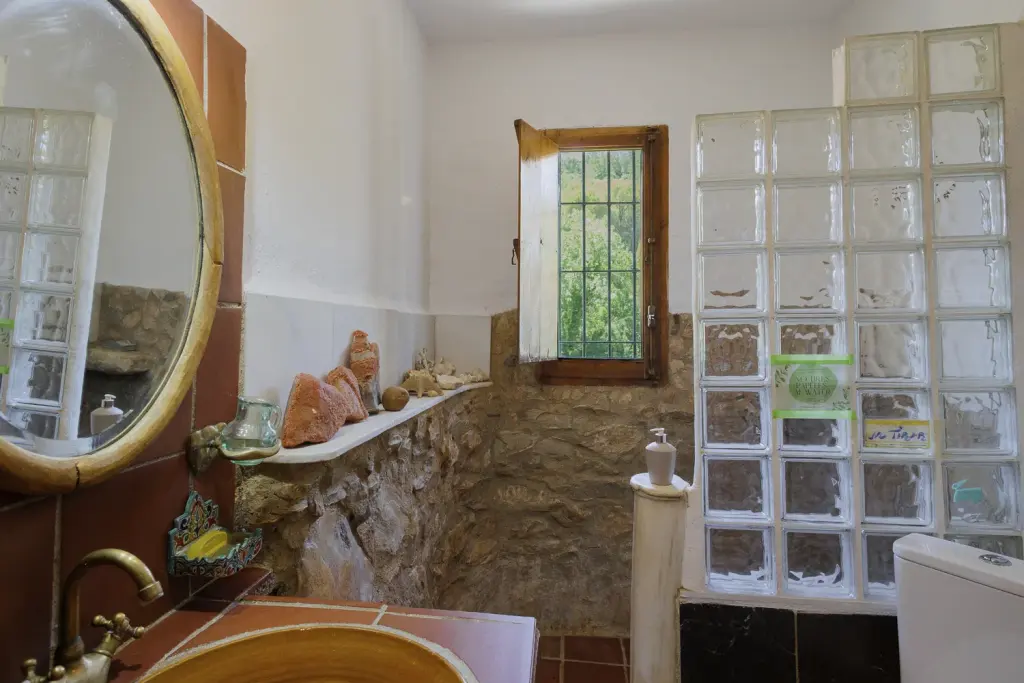 Baño con pared de pavés y ventana con vistas a la sierra