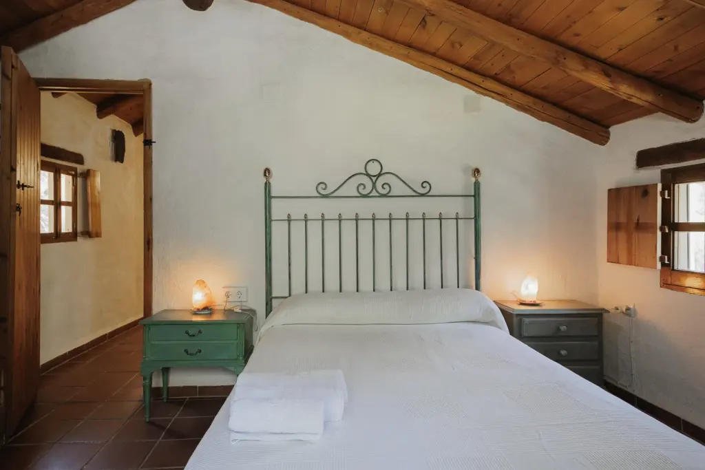 Dormitorio principal con cama de forja, mesillas verdes y vigas de madera