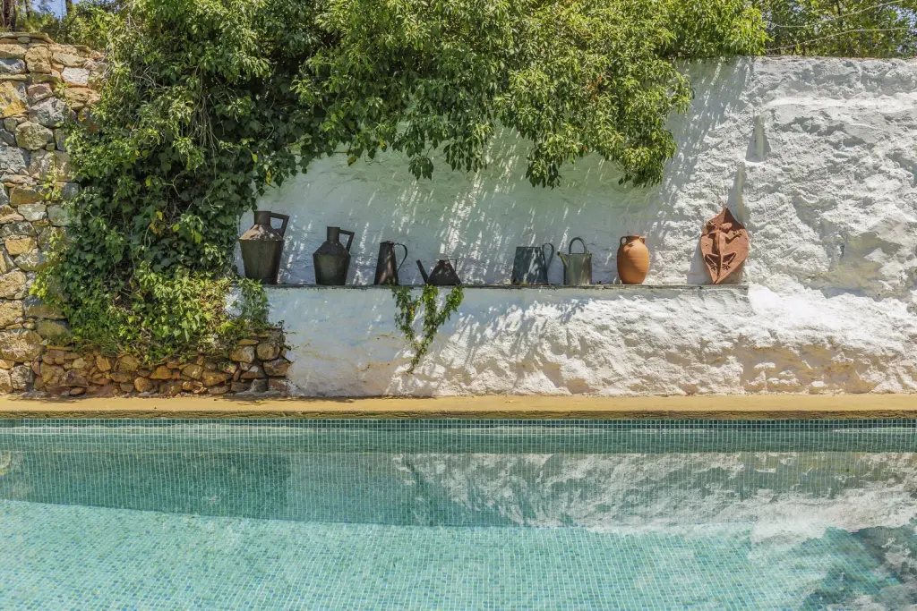 Piscina privada con muro encalado decorado con cántaros y hiedra