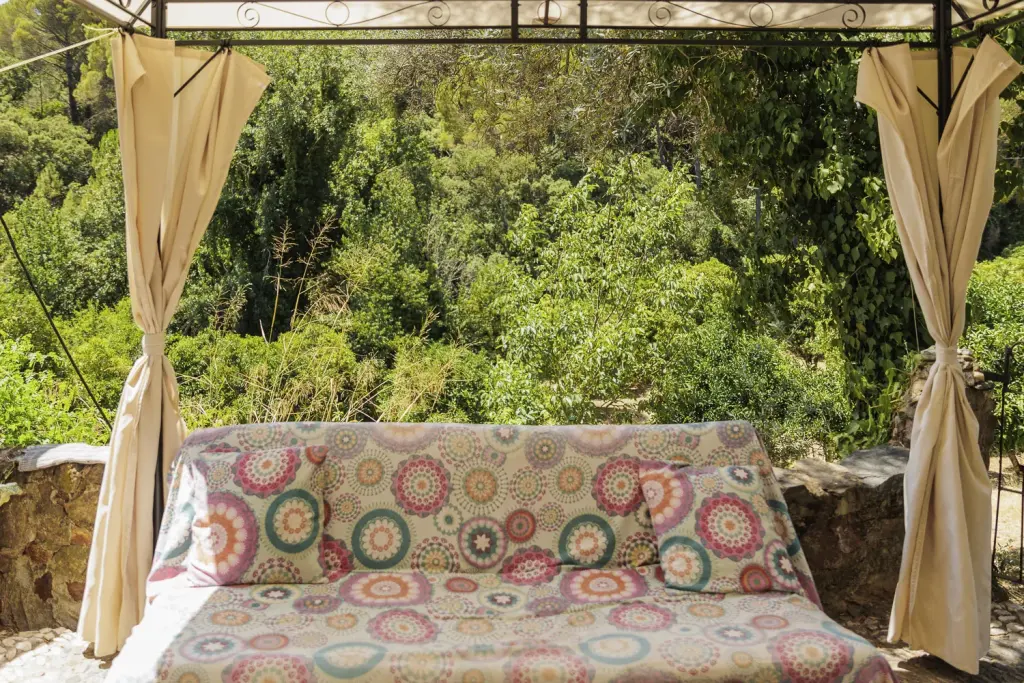 Cama balinesa con cojines de colores bajo el cenador, con vistas al bosque